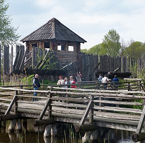 widok na most prowadzący do drewnianej wieży bramnej, po moście spacerują zwiedzający