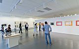 wnętrze centrum wystawienniczego: na białych ścianach zawieszone grafiki, w sali zwiedzający