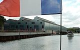 na pierwszym planie flaga francuska, w tle po lewej szara hala dla łodzi