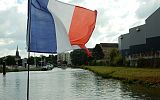 na pierwszym planie flaga Francji, w tle budynki mieszkalne i wieża kościoła