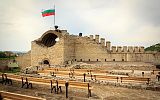 ruiny średniowiecznej twierdzy z zatkniętą flagą Bułgarii, na pierwszym planie cztery rzędy ławek