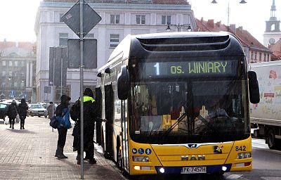 Autobus na przystanku. Na zdjęciu widać wchodzących ludzi i padający deszcz.
