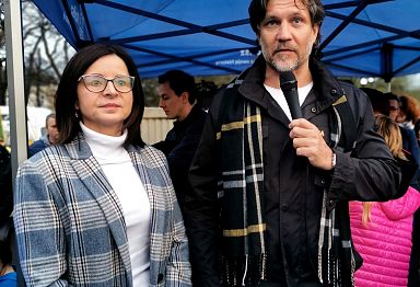 Prezydent Krystian Kinastowski przemawia przez mikrofon, obok kobieta w płaszczu