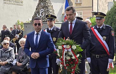 Wiceprezydent Mateusz Podsadny i prezydent Krystian Kinastowski składają wiązankę kwiatów, w tle strażnicy miejscy ze sztandarem