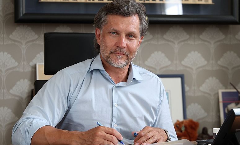 Prezydent Krystian Kinastowski w jasnej koszuli siedzi przy biurku, na którym leżą dokumenty