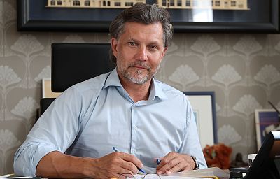Prezydent Krystian Kinastowski w jasnej koszuli siedzi przy biurku, na którym leżą dokumenty