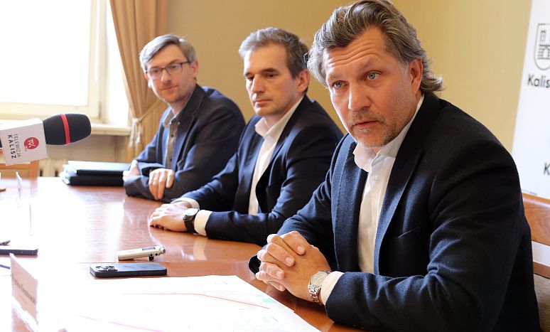 Uczestnicy konferencji ws. obwodnicy Kalisza ubrani w białe koszule i ciemne marynarki siedzą za drewnianym stołem i patrzą w stronę obiektywu.